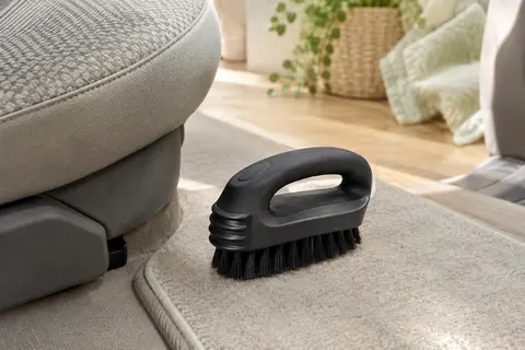 Brosse noire en caoutchouc posée près d’un siège automobile en tissu et d’un tapis clair