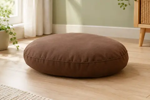 Coussin ovale marron en coton, posé sur un sol en bois clair dans un intérieur lumineux.
