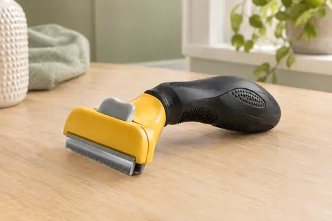 Outil Furminator noir avec bord en acier inoxydable, posé sur une surface en bois clair.