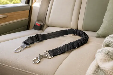 Sangle auto noire réglable pour chien avec partie élastique et mousqueton en aluminium sur une banquette.