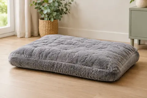 Coussin rectangulaire gris JOEJOY à surface matelassée, posé sur un sol en bois clair dans un intérieur lumineux.