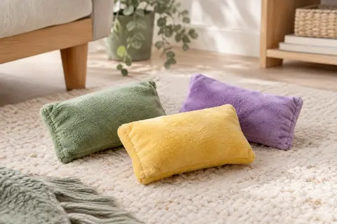 Trois coussins jouets pour chat en peluche verte, jaune et violette posés sur un tapis clair